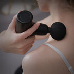 No More Sore mini massage gun in black being used on the shoulder