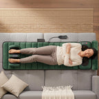 Woman lying on the green massage mat on a sofa, with her head on the pillow and her feet in the foot massager