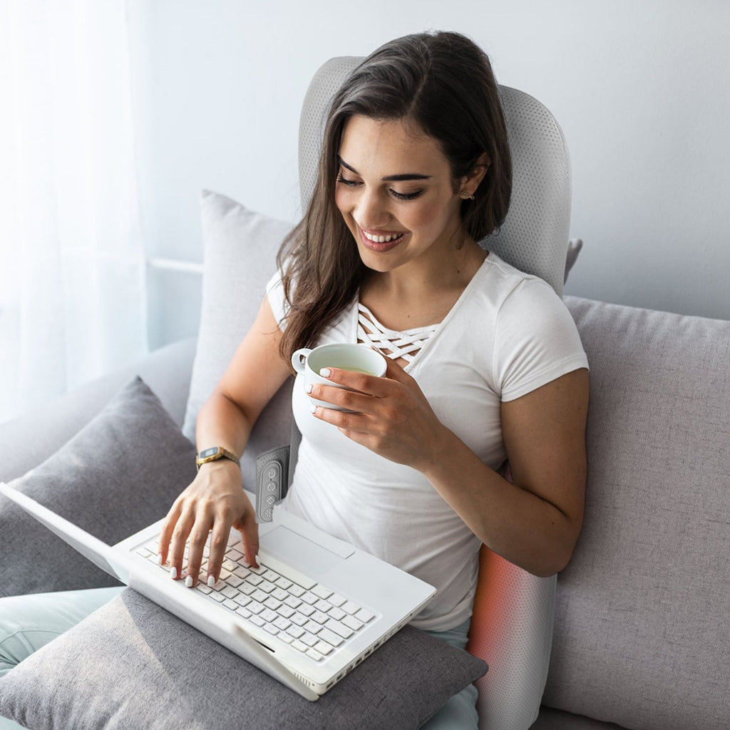 Woman using a laptop on a sofa with the back cushion behind her