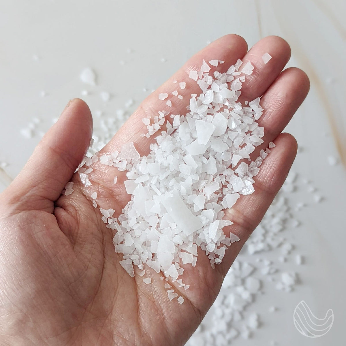 Hand holding a scoop of white Dead Sea magnesium flakes