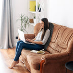 Woman using a laptop on a brown sofa with the massage cushion behind her