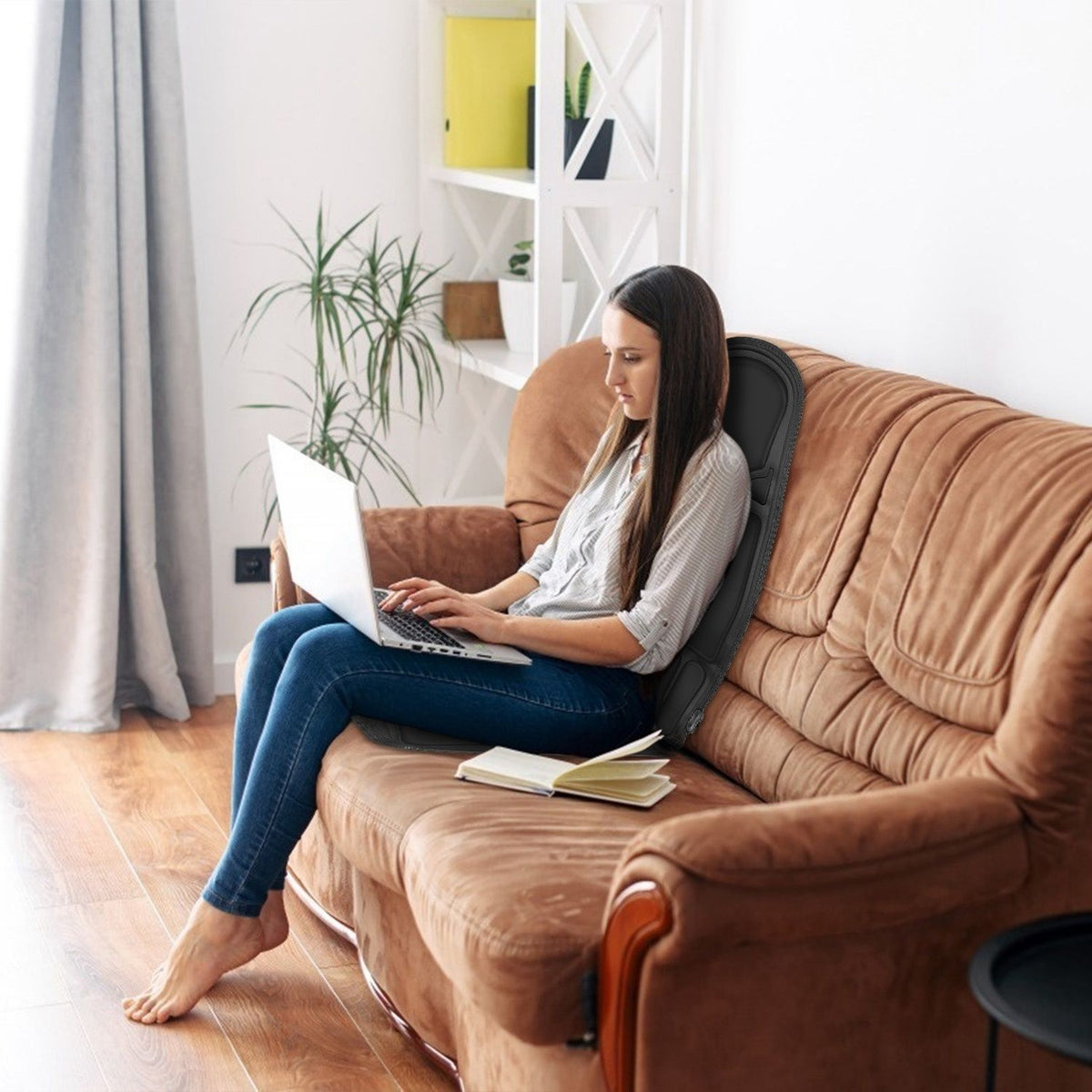 Woman using a laptop on a brown sofa with the massage cushion behind her