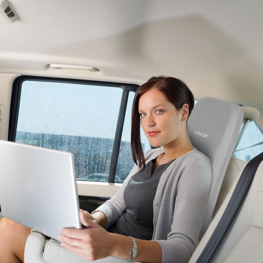 Woman using a laptop in a car seat with the back cushion behind her