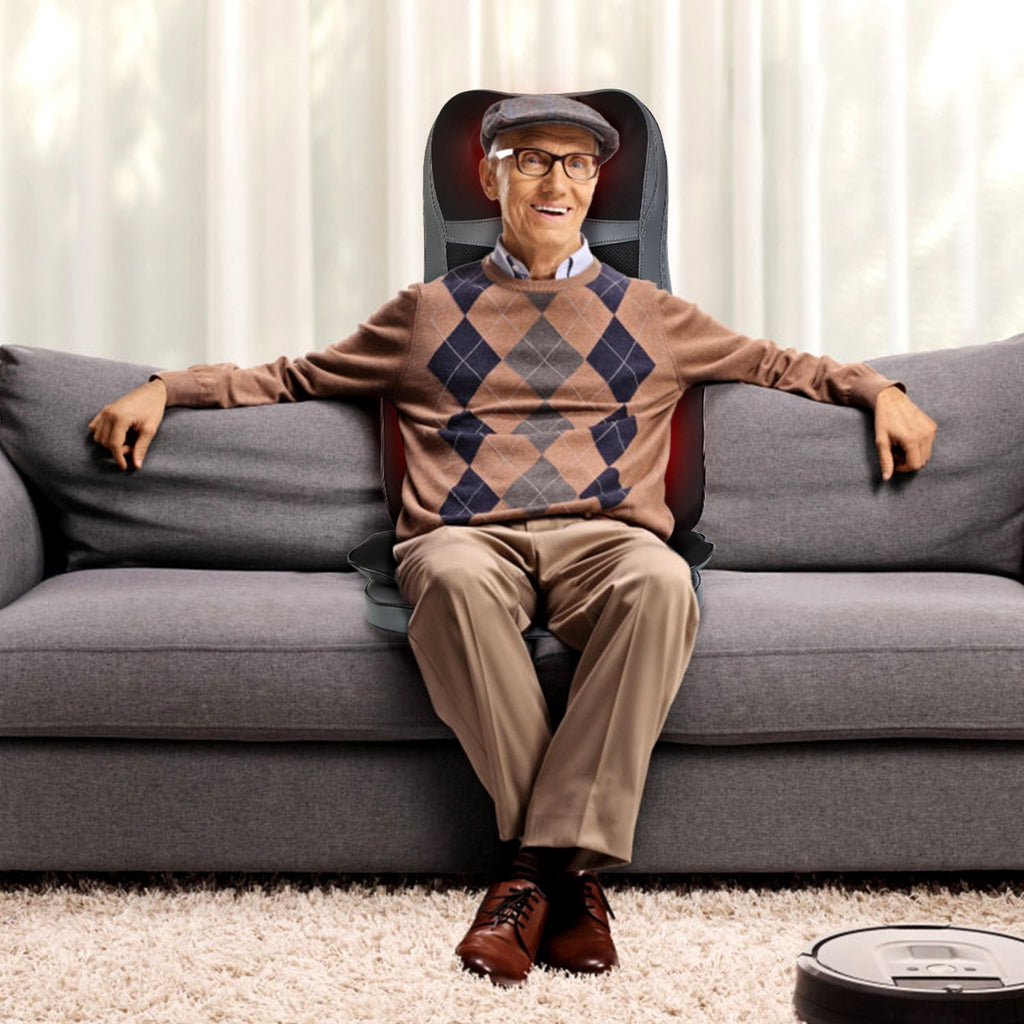 Older man sitting on a gray sofa with the massage cushion behind him