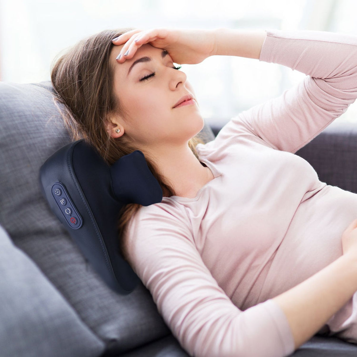 Woman lying on a sofa with the navy neck massager behind her neck
